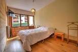 Cozy bedroom with wooden floors and walls, featuring a comfortable double bed and large windows offering scenic views.