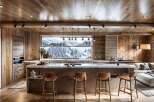 This stunning kitchen boasts a breathtaking view of a snow-capped mountain range through a large window, complemented by wood-paneled walls and ceilings.