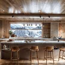 This stunning kitchen boasts a breathtaking view of a snow-capped mountain range through a large window, complemented by wood-paneled walls and ceilings.