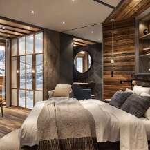 This luxurious hotel room boasts a stunning mountain view from its large windows and features a cozy, rustic design with wood paneling and a comfortable king-size bed.