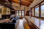 This charming chalet boasts a spacious open-plan living area with a large wooden dining table perfect for gatherings, a cozy fireplace for chilly evenings, and ample natural light from large windows showcasing stunning mountain views.