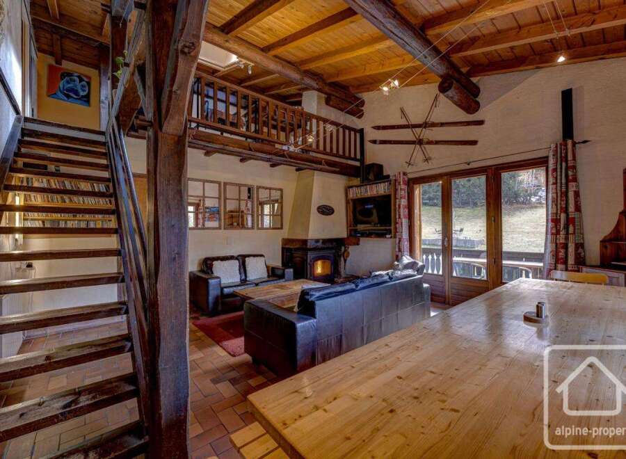 This charming chalet boasts a spacious open-plan living area with exposed wooden beams, a cozy fireplace, and large windows offering stunning views.