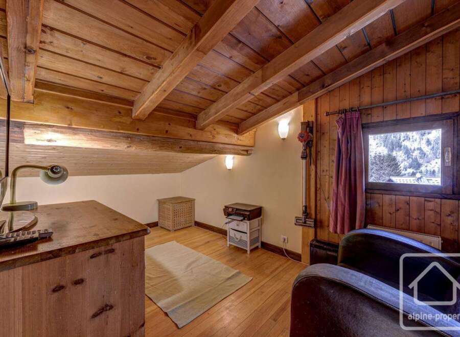 Cozy attic room with wood-paneled walls and ceiling, featuring a comfortable armchair, a wooden desk with a TV, and a small rug.