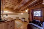 Cozy attic room with wood-paneled walls and ceiling, featuring a comfortable armchair, a wooden desk with a TV, and a small rug.