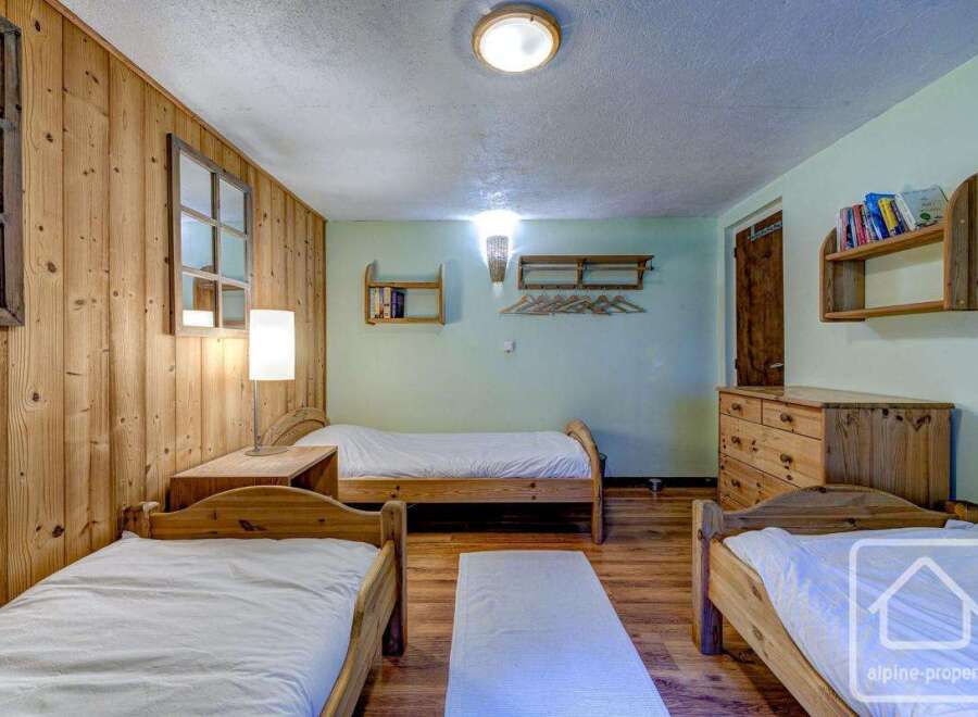 Cozy chalet bedroom with three single beds, wooden walls, and ample storage.