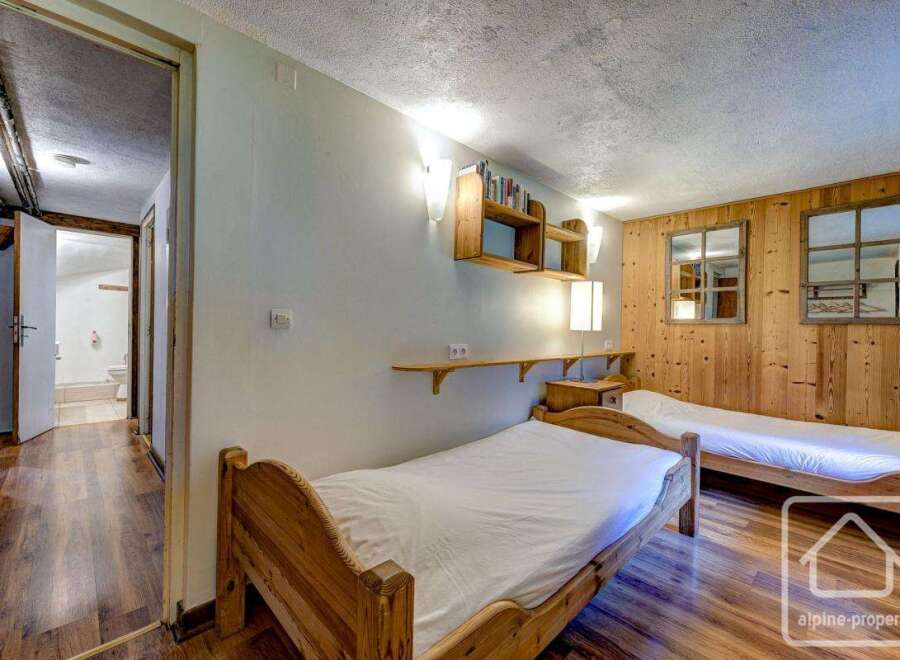 Cozy chalet bedroom with twin beds, wooden walls, and built-in shelves.
