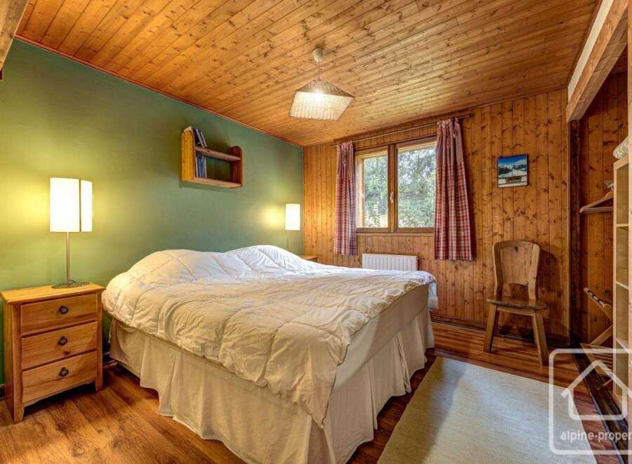 Cozy chalet bedroom with wooden walls and ceiling, featuring a comfortable double bed, bedside table, and ample closet space.
