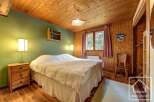 Cozy chalet bedroom with wooden walls and ceiling, featuring a comfortable double bed, bedside table, and ample closet space.