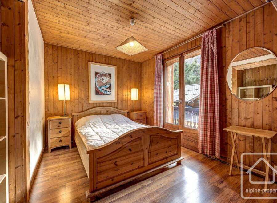 Cozy chalet bedroom with wooden walls and floors, featuring a comfortable double bed, built-in wardrobe, and a balcony with mountain views.