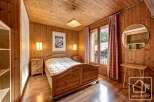 Cozy chalet bedroom with wooden walls and floors, featuring a comfortable double bed, built-in wardrobe, and a balcony with mountain views.