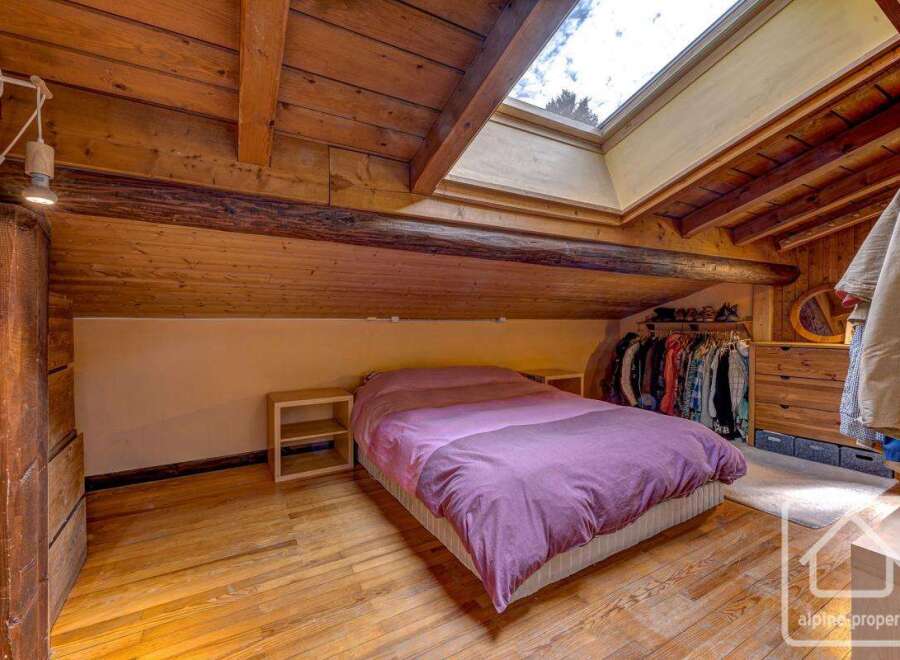 Charming attic bedroom with exposed wooden beams and skylights, offering ample natural light.