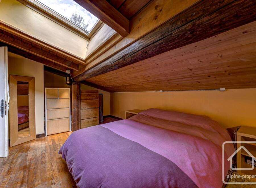 Cosy attic bedroom with wooden beams and skylights, offering a unique and charming atmosphere.
