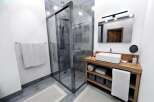Step into a modern bathroom oasis! This stunning space features a sleek glass shower, a stylish wooden vanity, and elegant tile flooring.