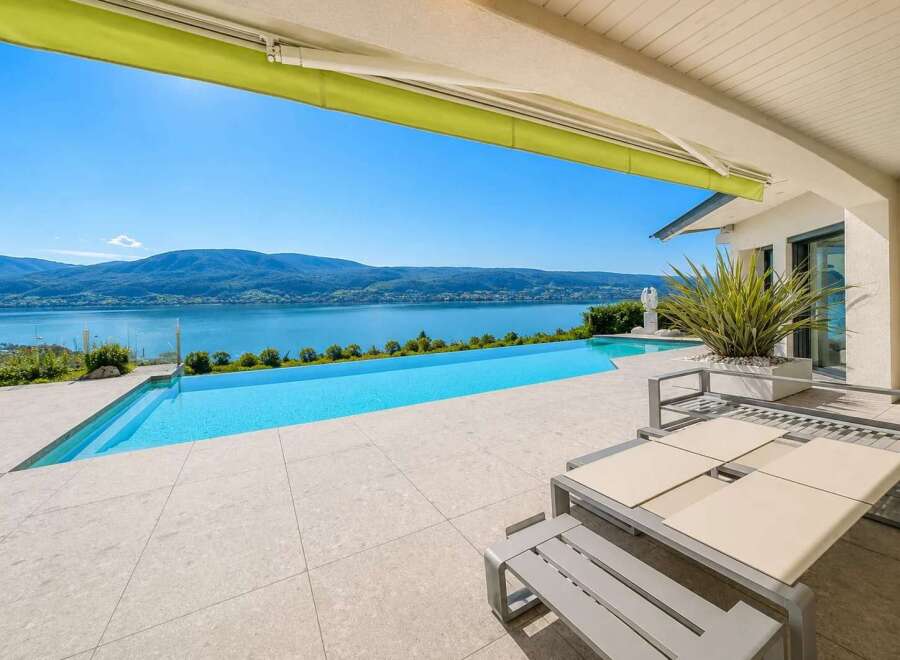 Experience luxury living with this stunning infinity pool overlooking a serene lake and majestic mountains.