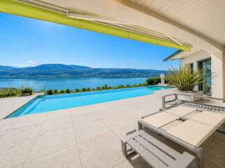 Experience luxury living with this stunning infinity pool overlooking a serene lake and majestic mountains.