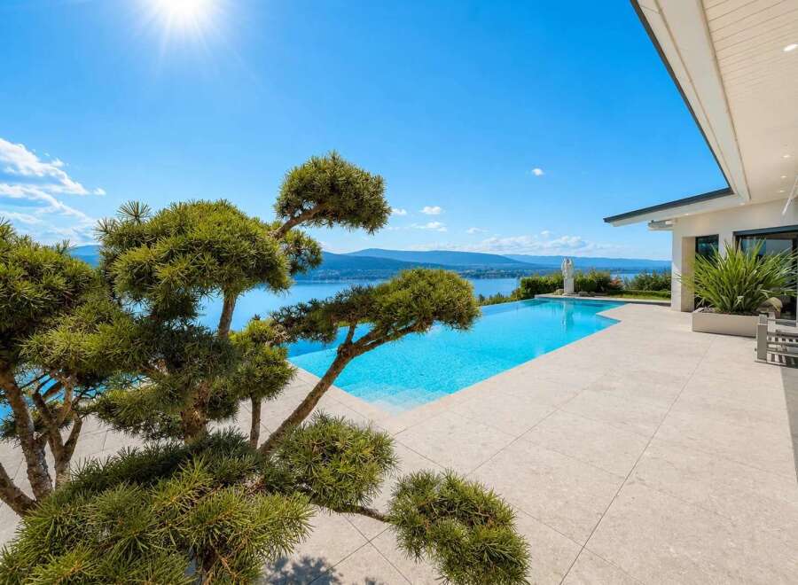 Experience luxury living with this stunning infinity pool overlooking a serene lake and majestic mountains.