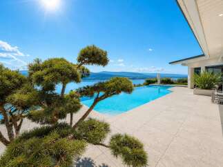 Experience luxury living with this stunning infinity pool overlooking a serene lake and majestic mountains.