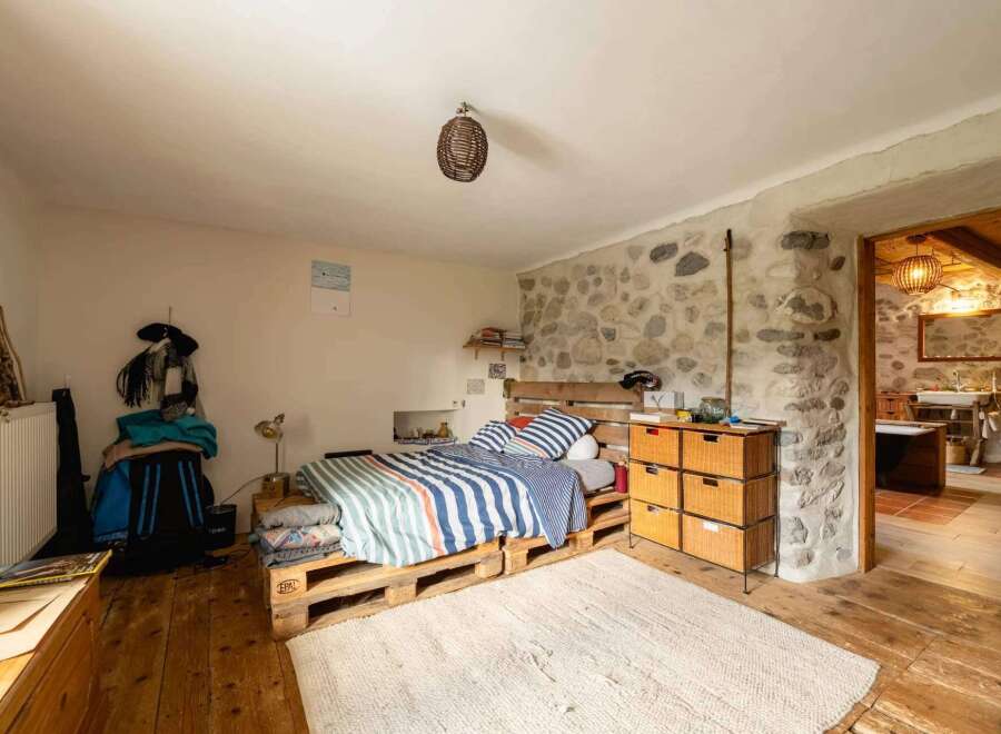 Rustic bedroom with pallet bed and stone wall.