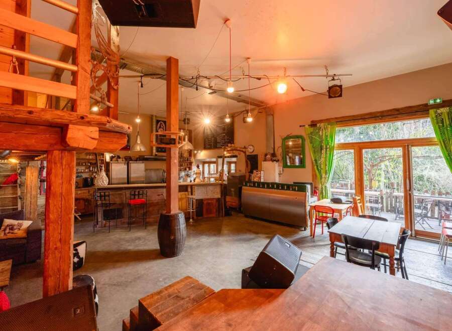 Rustic-chic bar with a spacious layout, featuring a wooden loft, large windows overlooking a patio, and ample seating.