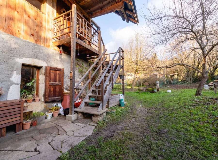 Rustic wooden staircase leading to a charming wooden balcony, nestled against a stone building.
