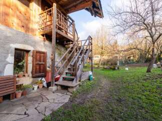 Rustic wooden staircase leading to a charming wooden balcony, nestled against a stone building.