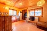 Cozy cabin with wooden ceilings and walls, featuring a kitchenette, living area, and large windows offering scenic views.