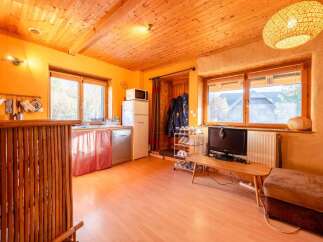 Cozy cabin with wooden ceilings and walls, featuring a kitchenette, living area, and large windows offering scenic views.