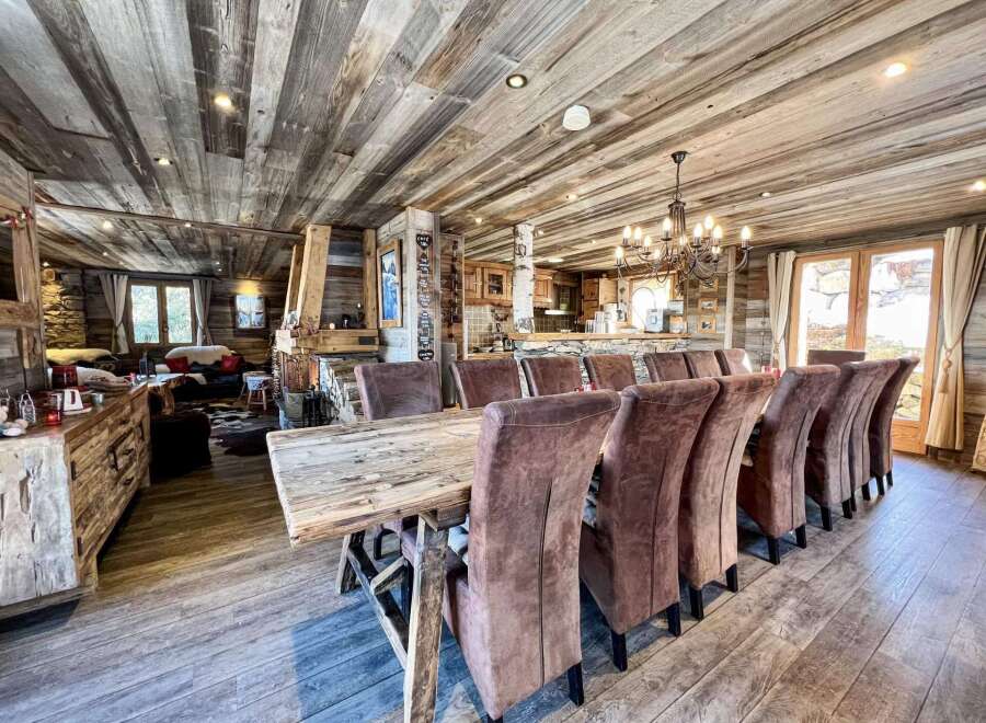 This stunning chalet boasts a spacious open-plan living area with a rustic wooden dining table and comfortable leather chairs, perfect for family gatherings.