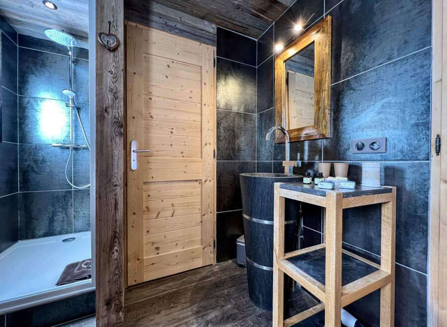 This stunning bathroom boasts a spacious shower, sleek dark tile, and a modern wooden vanity with a unique stone sink.