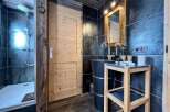 This stunning bathroom boasts a spacious shower, sleek dark tile, and a modern wooden vanity with a unique stone sink.