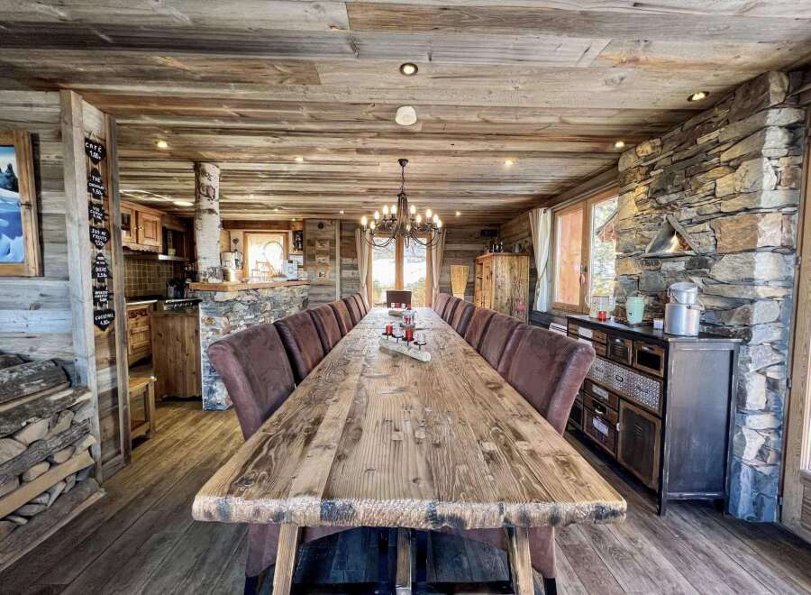 This stunning chalet boasts a magnificent, rustic dining table perfect for large gatherings, surrounded by comfortable leather chairs.