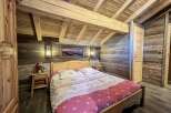 Cozy chalet bedroom with wooden beams, rustic walls, and a comfortable double bed.