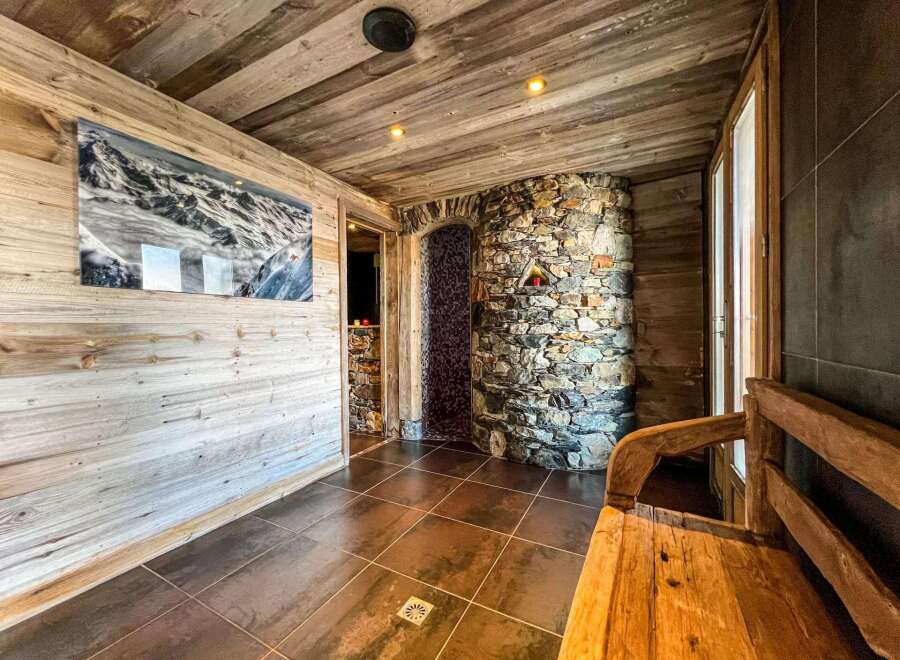 This luxurious chalet boasts a stunning spa area, complete with a rustic stone shower and a relaxing wooden bench.