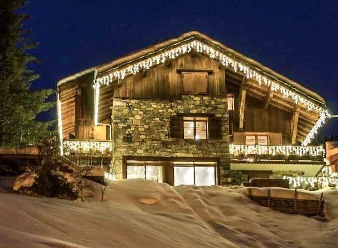 Luxury chalet nestled in the snowy mountains, featuring stunning nighttime views and charming exterior lighting.