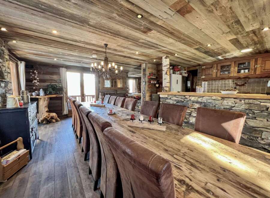 This stunning chalet boasts a magnificent reclaimed wood dining table perfect for large gatherings, surrounded by comfortable leather chairs.