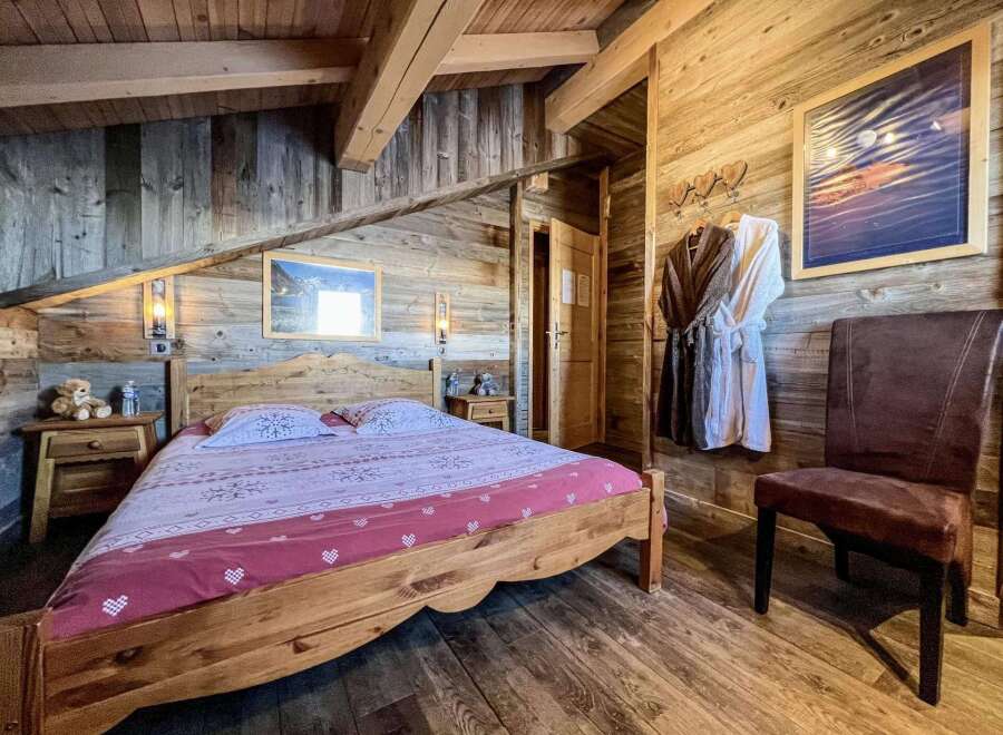 Cozy chalet bedroom with wooden walls and beams, featuring a comfortable double bed and plush bathrobes.