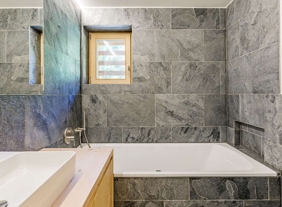 Discover a modern bathroom retreat featuring sleek gray tile and a luxurious soaking tub.