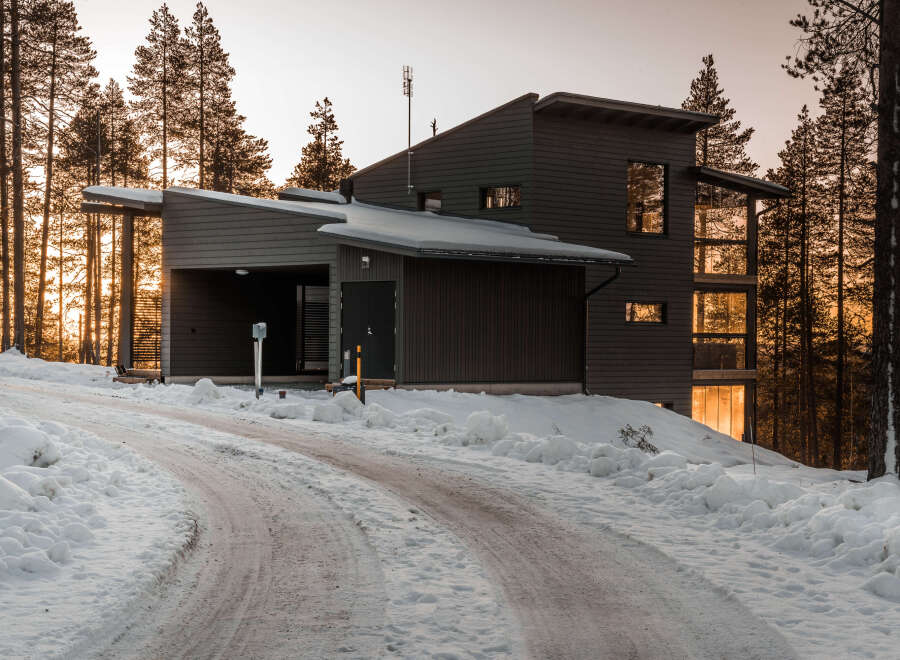 This modern home, nestled in a snowy landscape, showcases a sleek design with dark siding and large windows.