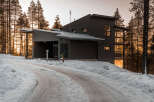 This modern home, nestled in a snowy landscape, showcases a sleek design with dark siding and large windows.