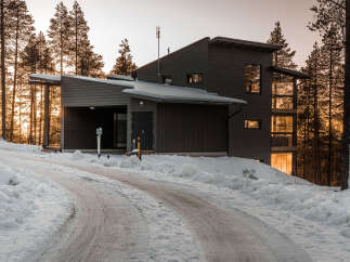 This modern home, nestled in a snowy landscape, showcases a sleek design with dark siding and large windows.