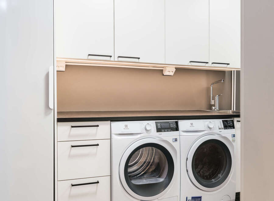 This modern laundry room features sleek white cabinetry and appliances, creating a clean and functional space.