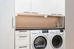 This modern laundry room features sleek white cabinetry and appliances, creating a clean and functional space.