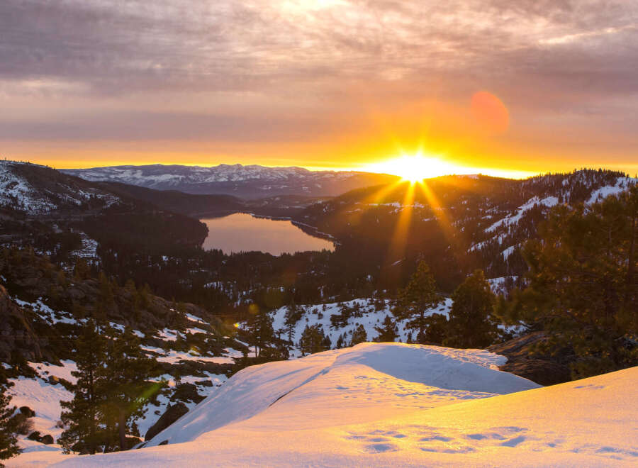 Spectacular sunrise over a snow-capped mountain range and serene lake.