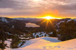 Spectacular sunrise over a snow-capped mountain range and serene lake.
