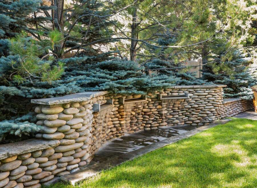This serene backyard oasis features a stunning stone waterfall, creating a tranquil ambiance.
