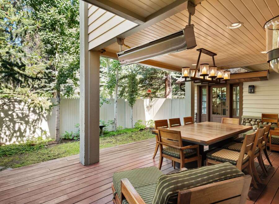 This stunning outdoor patio boasts a large wooden dining table, surrounded by comfortable wooden chairs with striped cushions, perfect for al fresco dining.