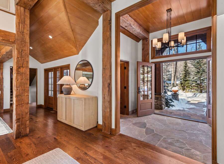 This stunning home boasts a grand entryway with reclaimed wood beams, hardwood floors, and a stone patio visible through French doors.