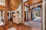 This stunning home boasts a grand entryway with reclaimed wood beams, hardwood floors, and a stone patio visible through French doors.