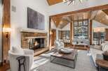 This stunning living room boasts a cozy stone fireplace, large windows offering breathtaking views, and a high ceiling with exposed wooden beams.
