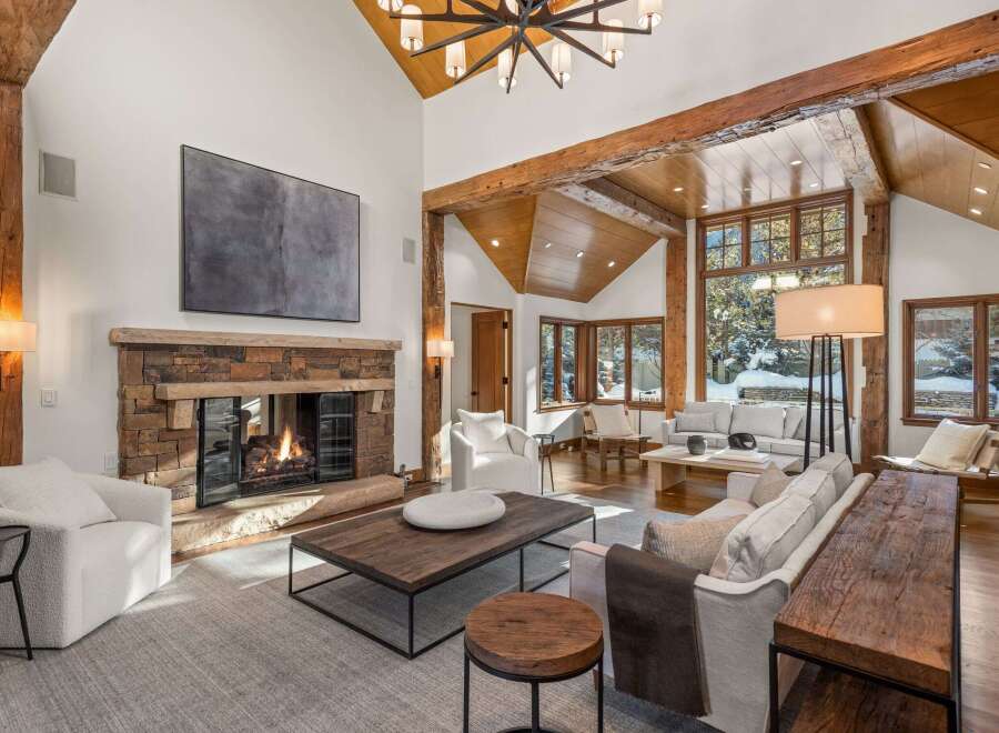 This stunning living room boasts a rustic-chic design with exposed wooden beams, a stone fireplace, and large windows offering breathtaking views.